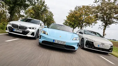 BMW i5 Touring, Porsche Taycan Sport Turismo und Audi A6 Avant e-tron fahren nebeneinander auf einer Landstraße, von vorne fotografiert. - Foto: Daniela Loof
