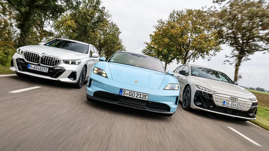 BMW i5 Touring/Porsche Taycan Sport Turismo/Audi A6 Avant e-tron BMW i5 Touring, Porsche Taycan Sport Turismo und Audi A6 Avant e-tron fahren nebeneinander auf einer Landstraße, von vorne fotografiert.
