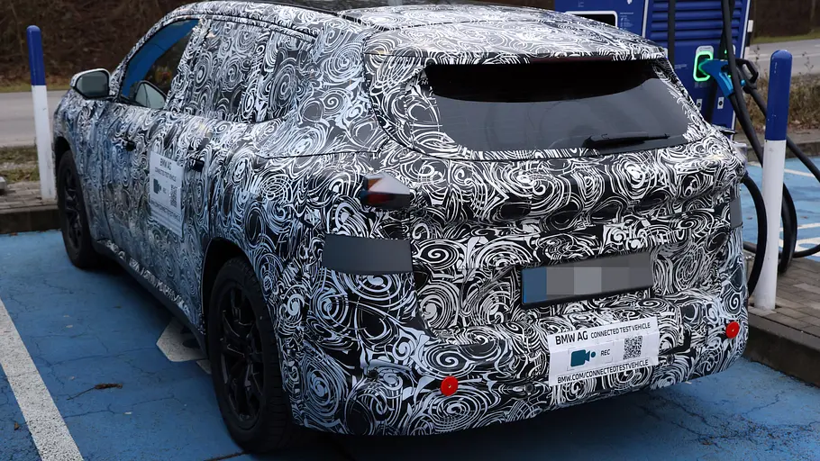 Als Erlkönig erwischt: Der BMW iX1 steht an einer Ladesäule, fotografiert von schräg hinten.
