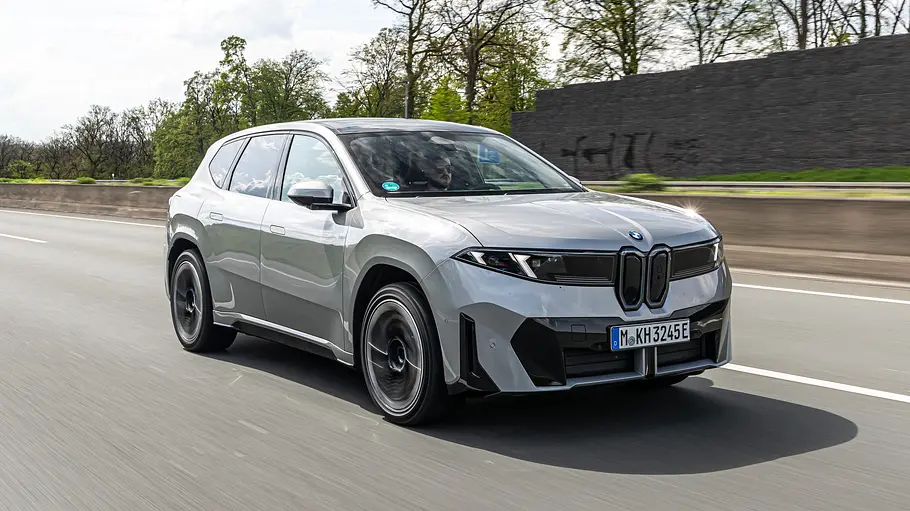 Ein silberner BMW iX3 fährt auf einer mehrspurigen Straße. Im Hintergrund stehen Bäume und eine Lärmschutzwand.