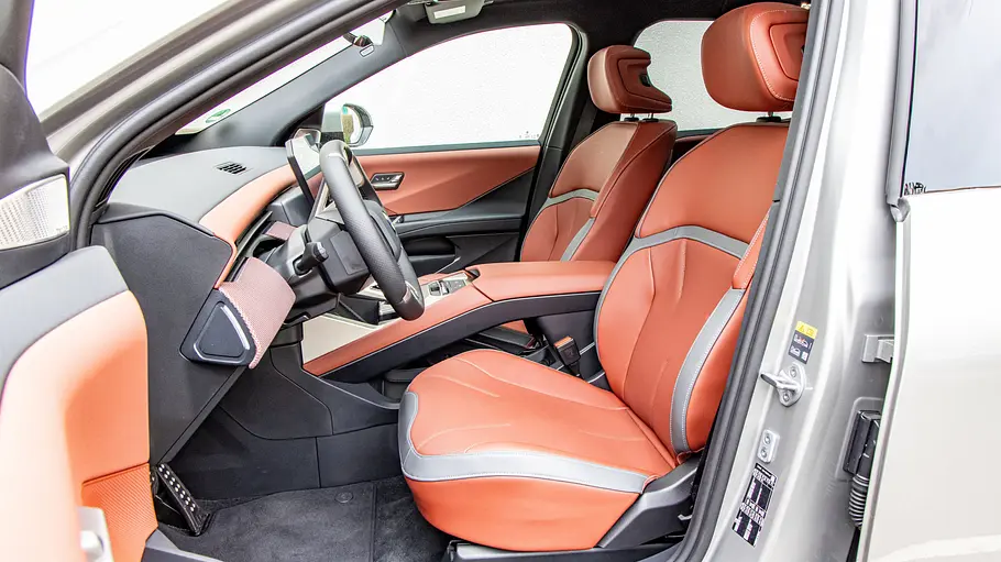 Die offene Fahrertür gibt den Blick auf orangefarbene Vordersitze, Lenkrad und Mittelkonsole eines BMW iX3 frei.