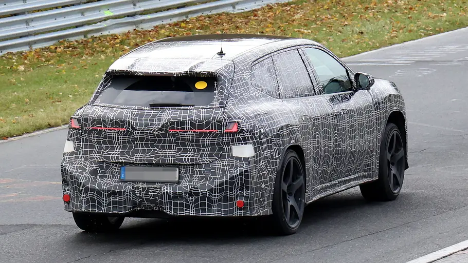 BMW iX3 M (2027) Der BMW iX3 (2027) fährt als Erlkönig auf der Nürburgring-Nordschleife, von hinten fotografiert.