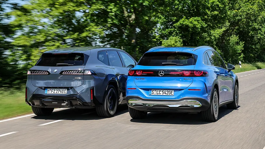 BMW iX3/Mercedes GLC EQ BMW iX3 und Mercedes GLC EQ fahren nebeneinander auf einer Landstraße, von hinten fotografiert.