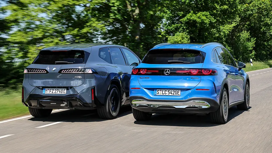 BMW iX3/Mercedes GLC EQ BMW iX3 und Mercedes GLC EQ fahren nebeneinander auf einer Landstraße, von hinten fotografiert.