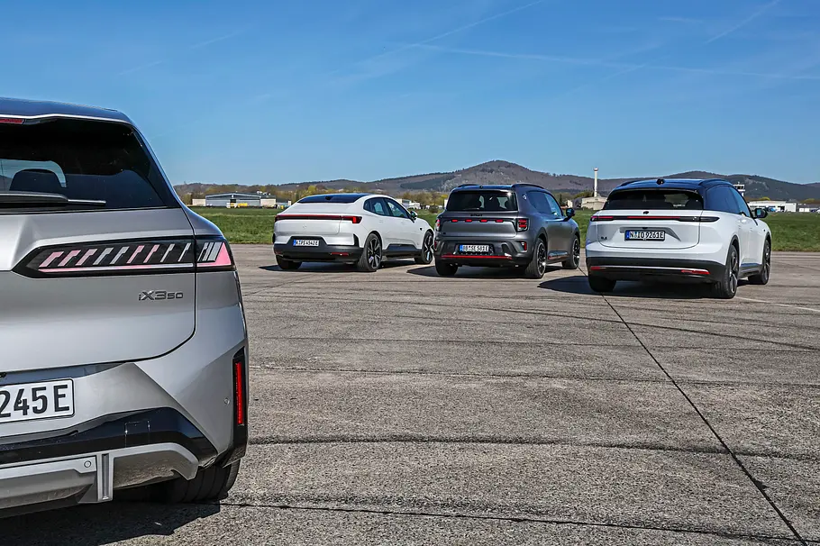 Vergleichstest BMW iX3, Polestar 4, Nio EL6 und Smart #5 BMW iX3, Polestar 4, Nio EL6 und Smart #5 stehen nebeneinander auf einer breiten Asphaltstrecke. Ein silberner BMW steht im Vordergrund unter blauem Himmel.