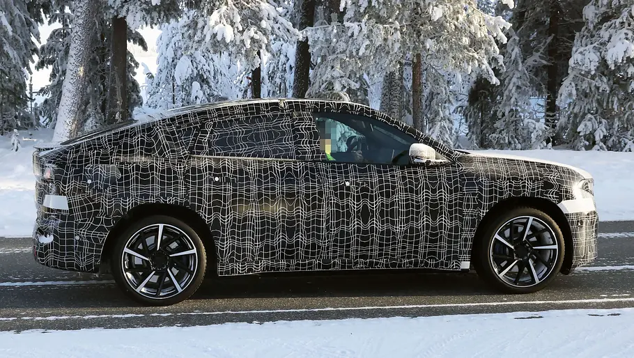 Der BMW iX4 fährt als Erlkönig durch eine verschneite Landschaft, von rechts fotografiert.