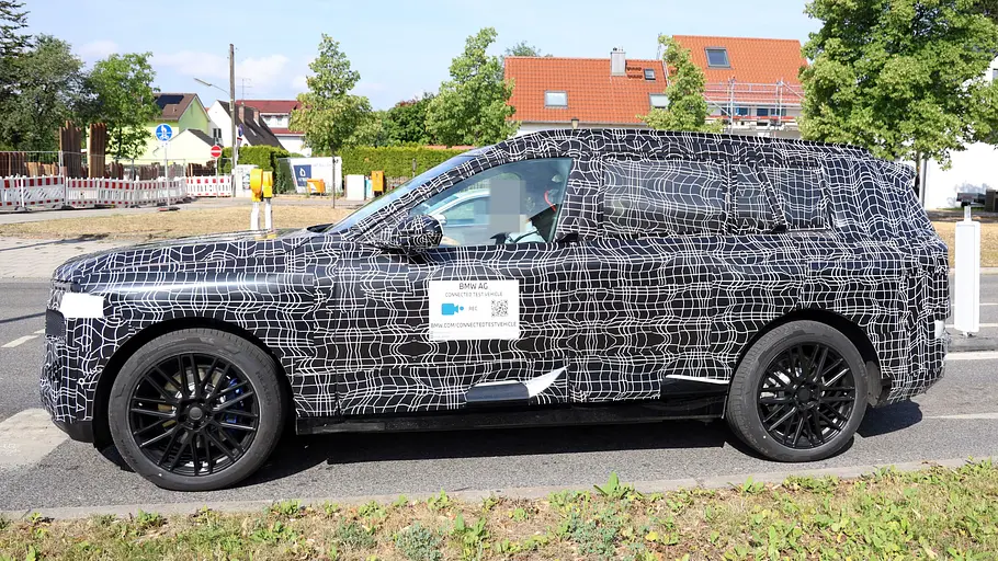 Der BMW iX7 fährt als Erlkönig auf der Straße, von links fotografiert.