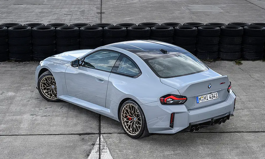 BMW M2 CS (2025) Der BMW M2 CS (2025) stehend auf grauem Asphalt und vor einer Wand aus gestapelten Reifen. Aus einer Vogelperspektive.