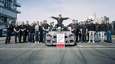 BMW M2 CS mit Nordschleifen-Rekord: Bild zeigt das gesamte Team rund um Rennfahrer Jörg Weidinger, der auf der Motorhaube des BMW M2 CS sitzt. - Foto: BMW