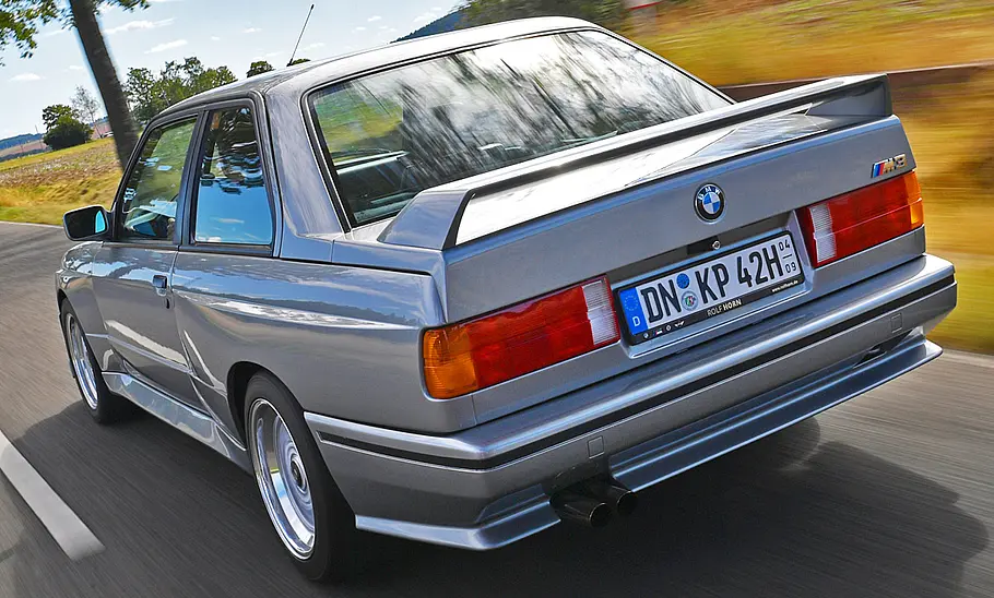 Der BMW M3 E30 fahrend von schräg hinten fotografiert.