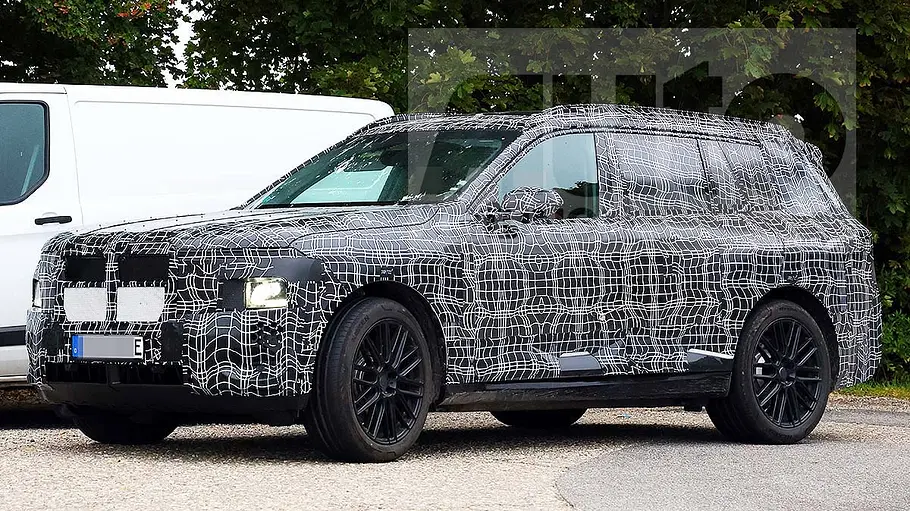 Der BMW iX7 (2027) steht als Erlkönig auf einem Parkplatz, von vorne rechts fotografiert.