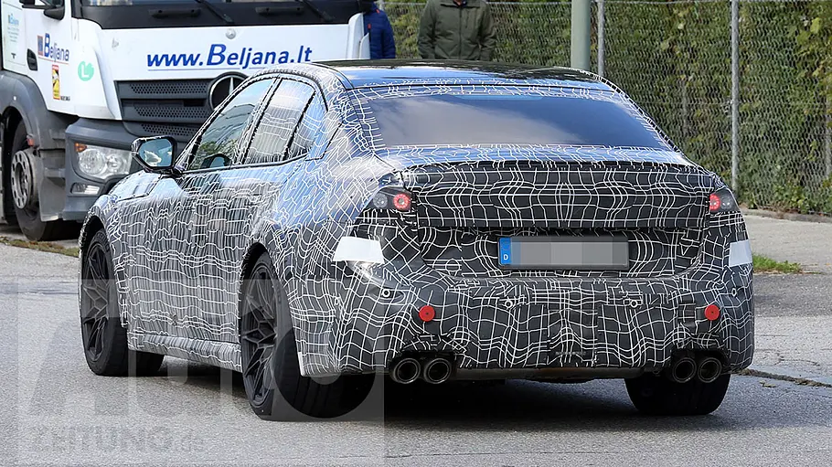 Der BMW M3 (2027) fährt als Erlkönig durch eine Ortschaft, von hinten links fotografiert.