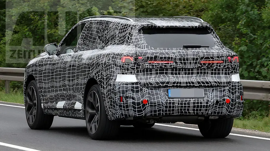 BMW (i)X5 (2026) Der BMW X5 (2026) fährt als Erlkönig auf einer Landstraße, von hinten links fotografiert.