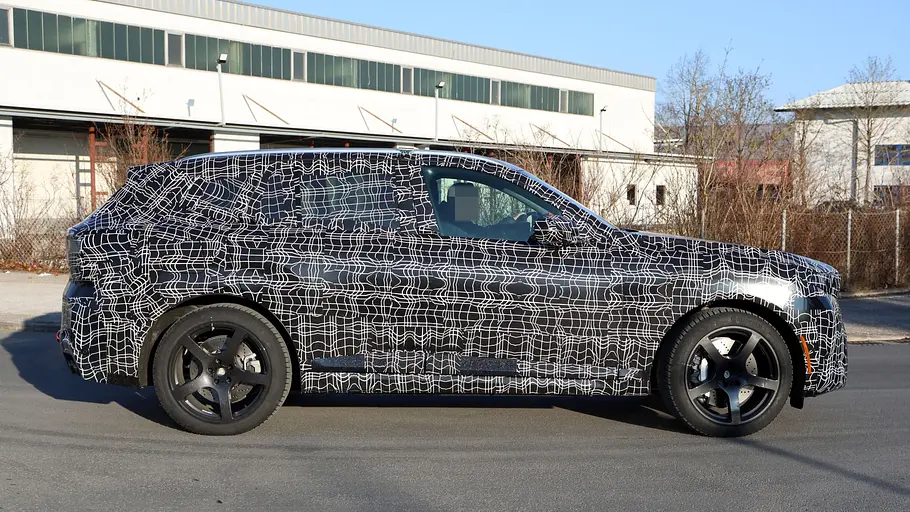 BMW X5 M60e Der BMW X5 M60e fährt als Erlkönig durch eine Stadt, von rechts fotografiert.