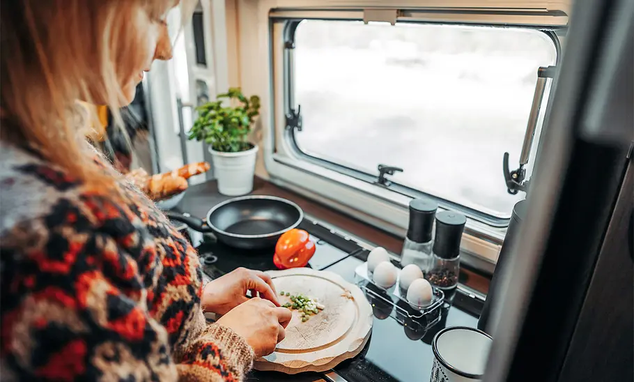 Bürstner Lineo T 690 G (2024): Das Innenraumfoto zeigt eine Person beim Zubereiten einer Mahlzeit.