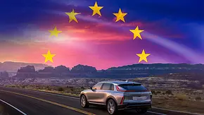 Ein Cadillac fahrend auf einer Straße, man sieht das Fahrzeug von hinten. Am Horizont geht die Europafahne auf. - Foto: AUTO ZEITUNG (KI-generiert)