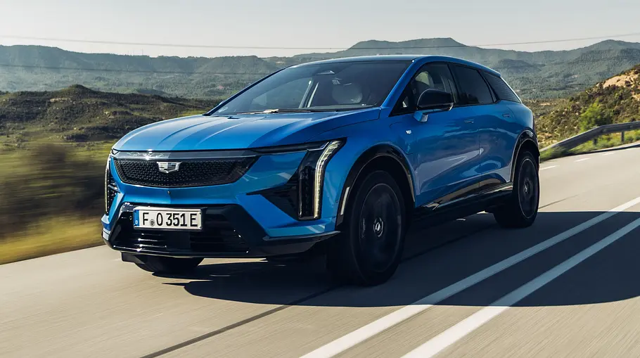 Der Cadillac Optiq (2026) fährt auf einer Landstraße. Fotografiert von schräg vorne.