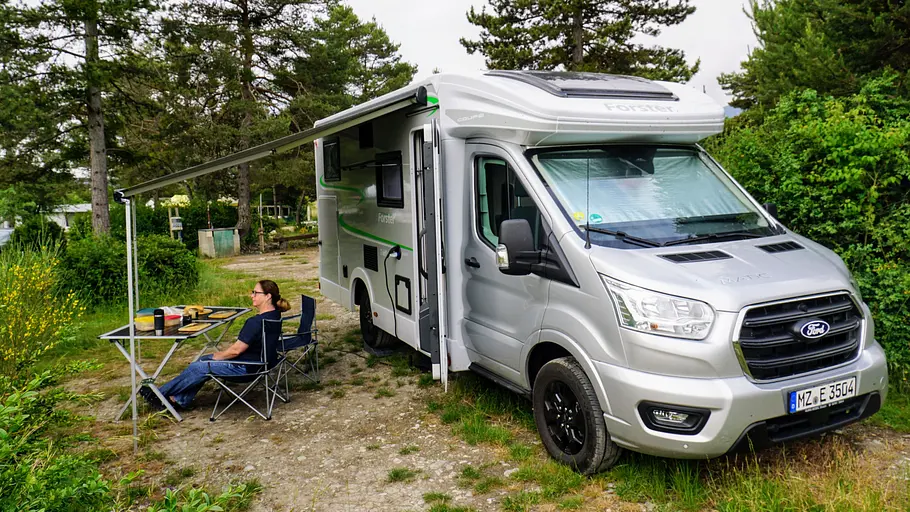 Der Forster T 669 EB auf einem Campingplatz mit ausgefahrener Markise und aufgebauten Campingmöbeln.
