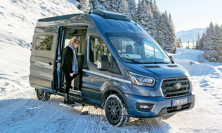 Der Carado CV590 4x4 ist mit Ansicht von schräg vorne stehend im Schnee zu sehen. Eine Person steigt durch die Schiebetüre ein.