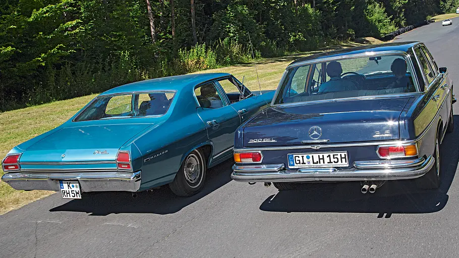 Chevrolet Chevelle und Mercedes 300 SEL 3.5 fahren auf einer Straße nebeneinander. Ansicht von hinten.