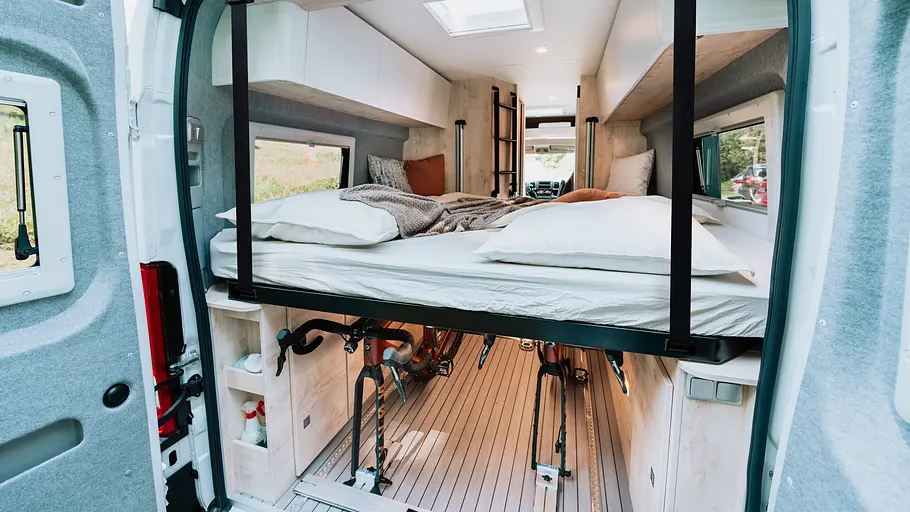 Clever Vans Runner 636 Active Die Aufnahme von außen nach innen zeigt das Hubbett im Mittelposition und die darunter liegenden Heckgarage bei geöffneten Seitentüren.