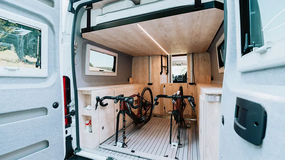Clever Vans Runner 636 Active Die Aufnahme von außen nach innen zeigt das bis unter die Decke hochgefahrene Hubbett und die darunter liegenden Heckgarage bei geöffneten Seitentüren.
