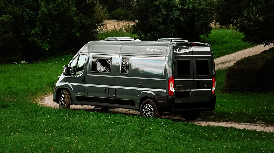Der Clever Vans Spirit 600 statisch von schräg hinten links. Der Campervan steht in einer Kurve auf einer schmalen Staubpiste.