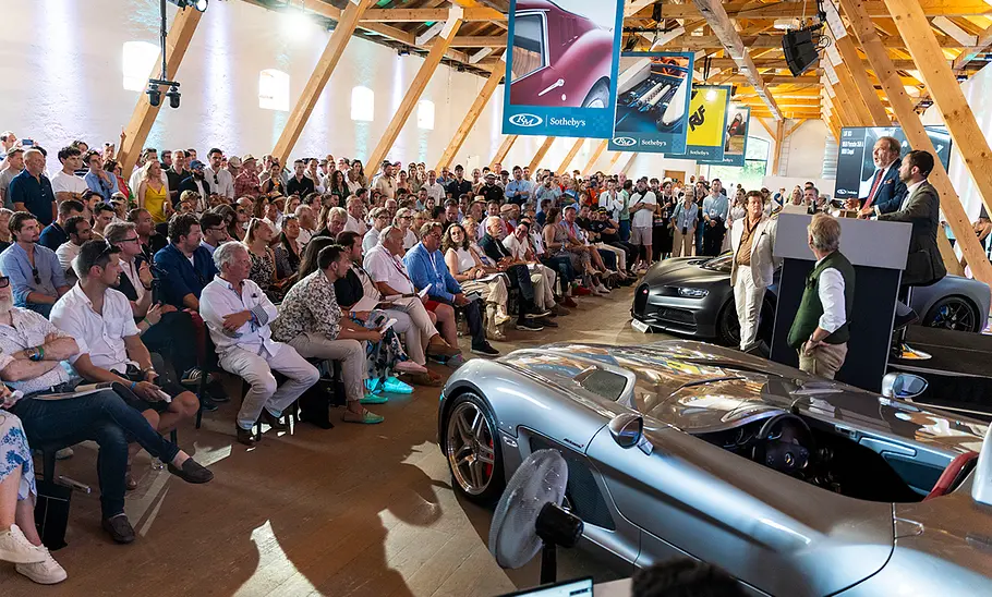 Die Sotheby’s Versteigerung auf den Concours of Elegance 2024. Vor Fahrzeugen sitzen viele Menschen, die sich an der Auktion beteiligen oder zuschauen.