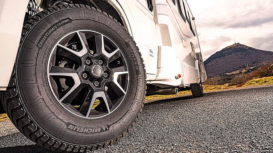 Reifen für Wohnmobile Das Bild zeigt ein Wohnmobil von schräg unten links fotografiert. Der Fokus liegt auf dem leicht eingeschlagenen Vorderrad, auf dem ein Reifen für Wohnmobile installiert ist.