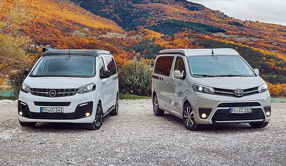 Das Bild zeigt die beiden Basisfahrzeuge des Crosscamp Urban Camper stehend von schräg vorne. Links steht der Opel Zafira Life, rechts der Toyota Proace Verso.
