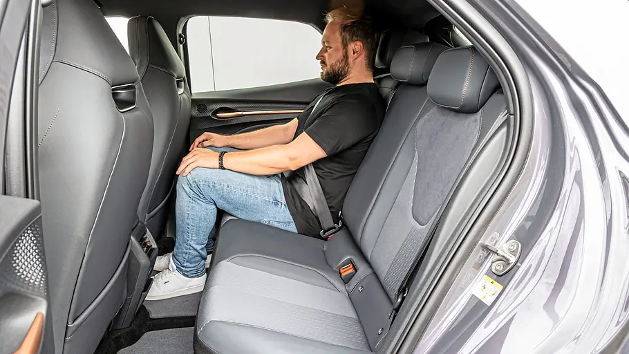 Mann sitzt im Fond des Cupra Raval Endurance auf der Rücksitzbank, Blick auf Kniefreiheit und Kopfraum