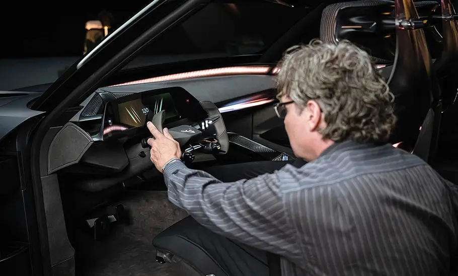 Ein Redakteur der AUTO ZEITUNG kniet auf der Studioaufnahme vor der geöffneten Fahrertür des Cupra Tindaya und befühlt das Lenkrad.