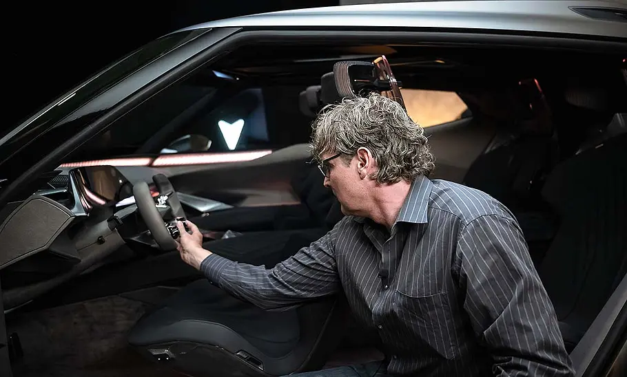 Ein Redakteur der AUTO ZEITUNG kniet vor der IAA-Konzeptstudie Cupra Tindaya (2025) bei geöffneter Fahrertür und hat eine Hand am Lenkrad.
