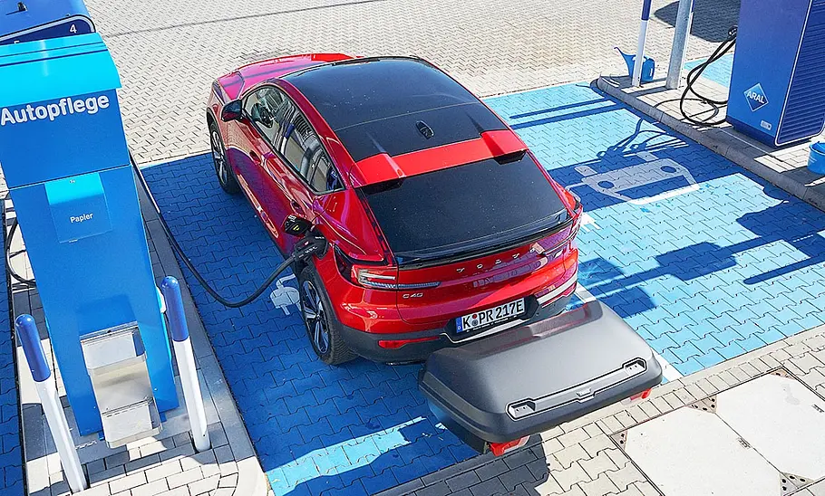 Das Bild zeigt einen Volvo C40 Recharge Pure Electric von schräg hinten links an einer Ladesäule für Elektroautos. Das Foto ist aus einer leicht erhöhten Position aufgenommen. Eine Heckbox ist auf der Anhängerkupplung angebracht.