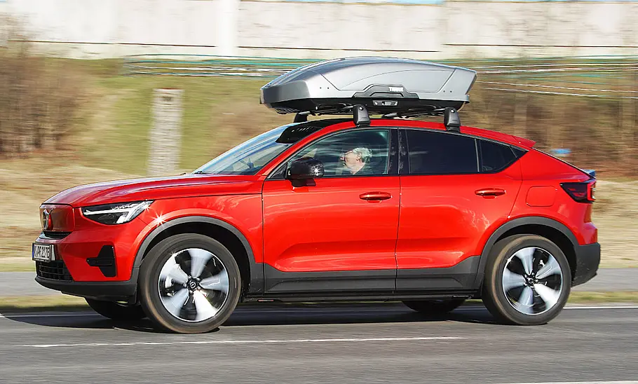 Das Bild zeigt den Volvo C40 Recharge Pure Electric fahrend von schräg vorne links. Eine Dachbox ist auf Dachträgern angebracht.