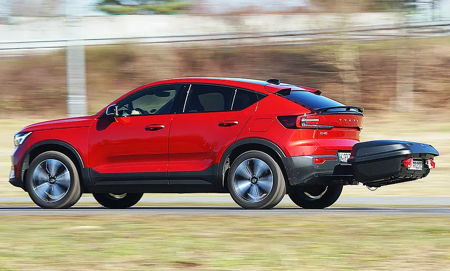 Das Bild zeigt den Volvo C40 Recharge Pure Electric fahrend von schräg hinten links. Eine Heckbox ist auf der Anhängerkupplung angebracht.