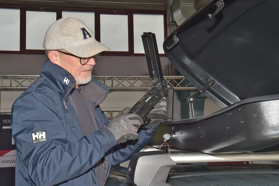 Farad Marlin im Dachboxen-Test Ein Testredakteur hält einen Befestigungsschlitten für eine Dachbox in den Händen.