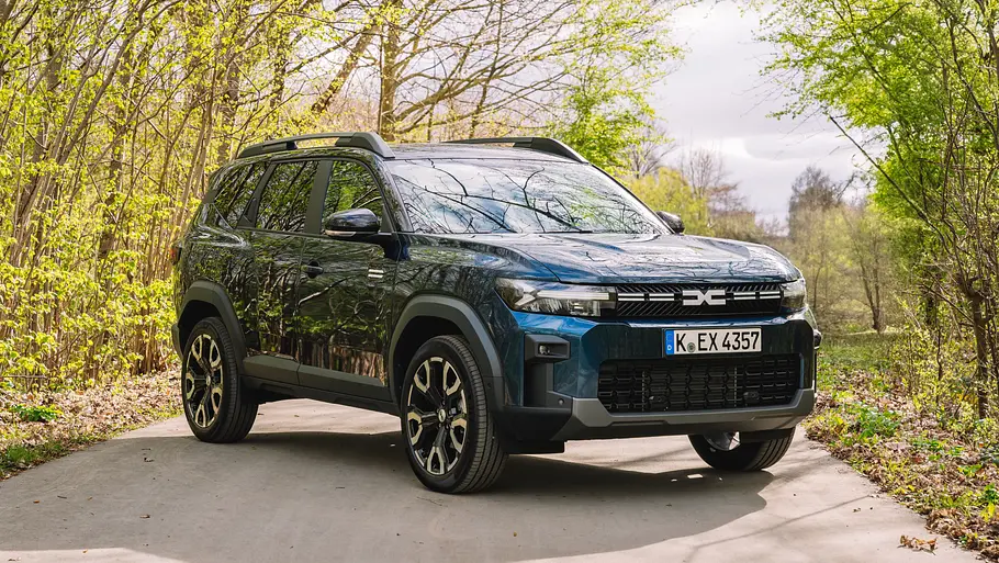 Dacia Bigster Der Dacia Bigster schräg auf einem Feldweg zwischen Bäumen und Sträuchern stehend von vorne links.