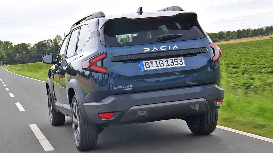 Der Dacia Bigster fährt auf einer Landstraße, von hinten links fotografiert.