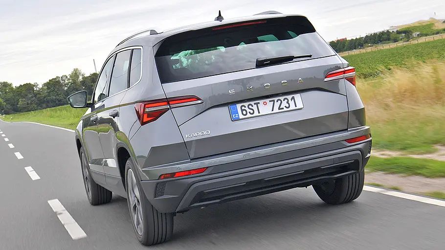 Der Skoda Karoq fährt auf einer Landstraße, von hinten links fotografiert.