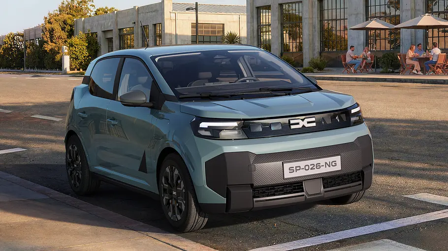 Der Dacia Spring steht am Straßenrand. Gegenüber sitzen Menschen vor einem Betongebäude unter Sonnenschirmen.