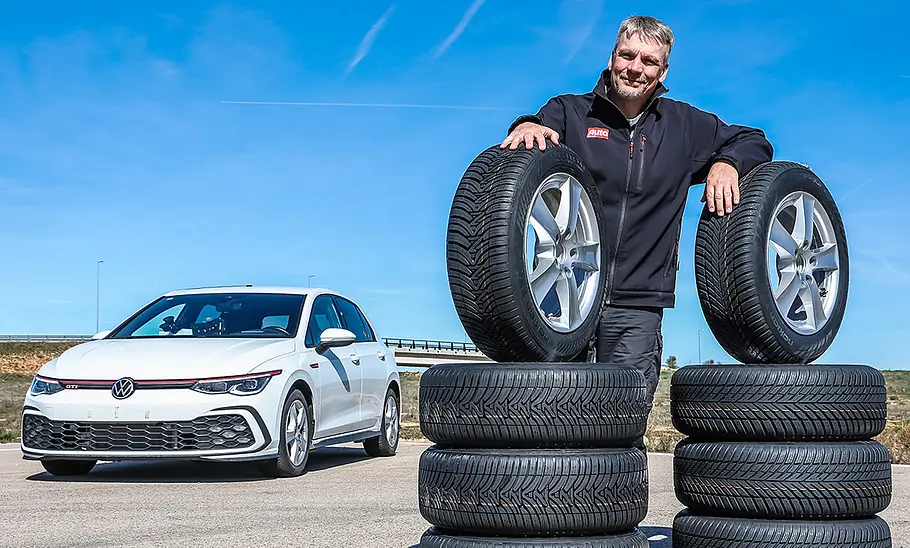 Redakteur Martin Urbanke posiert stolz hinter einem Stapel Reifen, im Hintergrund steht der Testwagen VW Golf GTI.