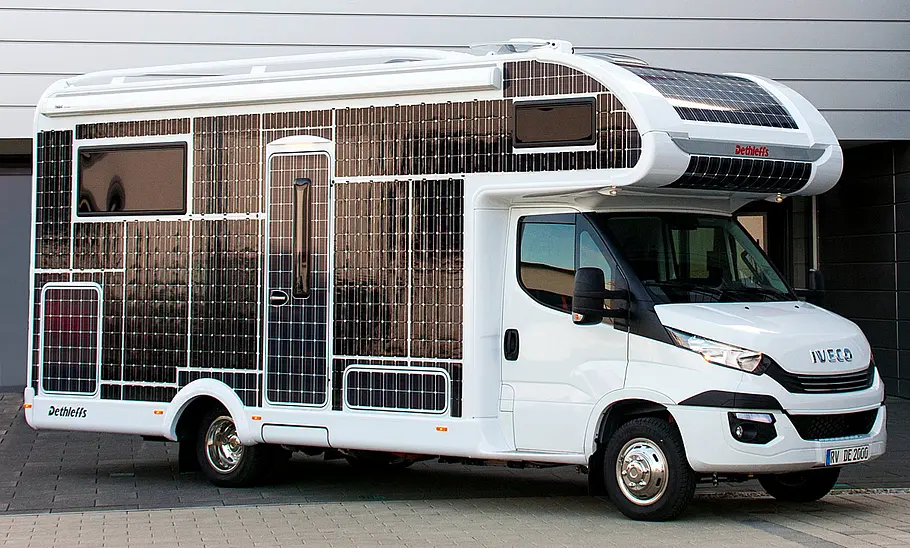 Dethleffs E.Home (2017) steht vor einem Geschäftsgebäude, die Seiten des Wohnmobils sind flächendeckend mit Solarfolie beklebt, Ansicht von der rechten Seite.