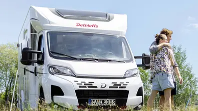 Ein Paar steht vor einem frontal seitlich aufgenommenen Dethleffs Just Camp T 6762 (2025). - Foto: Dethleffs
