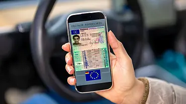 Detailaufnahme von einer Hand, die ein Smartphone hält, auf dem ein Führerschein abgebildet ist. - Foto: Imago