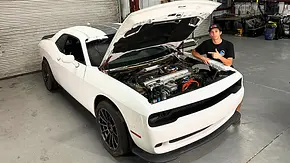 Blick von schräg vorne auf den Dodge Challenger mit Tesla-Technik von BoostedBoiKyle. Die Motorhaube ist geöffnet, eine Person posed neben dem Auto. - Foto: Boostedboikyle via Instagram