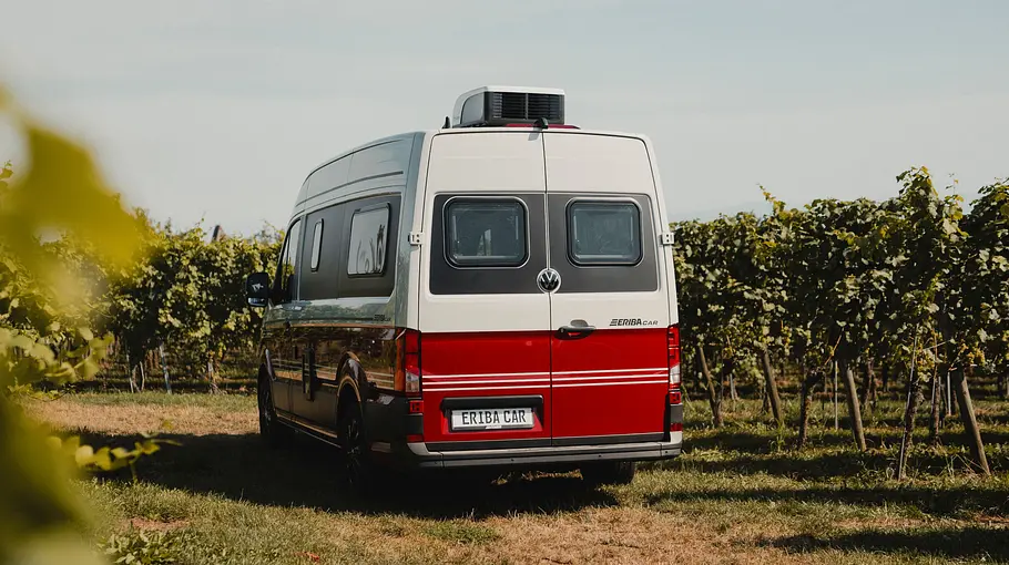 Der Eriba Car statisch von schräg hinten links vor Weinreben auf einer Wiese parkend.
