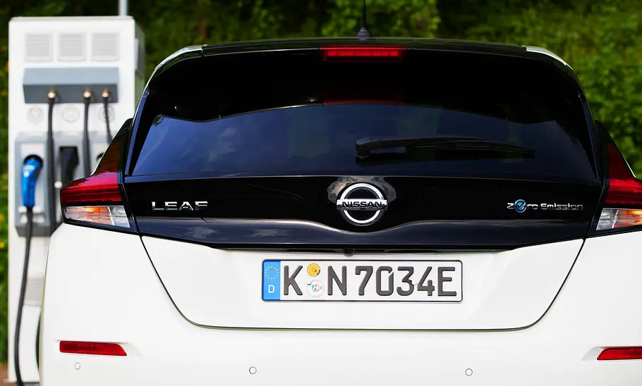 Das Heck des Nissan Leaf mit Blick auf das Kennzeichen, im Hintergrund steht eine Ladesäule.