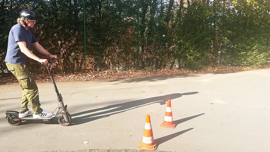 E-Scooter Segway Ninebot F3 Pro D Die Außenaufnahme zeigt einen Testredakteur auf dem E-Scooter Segway Ninebot F3 Pro D, der frontal auf zwei Hütchen zufährt.