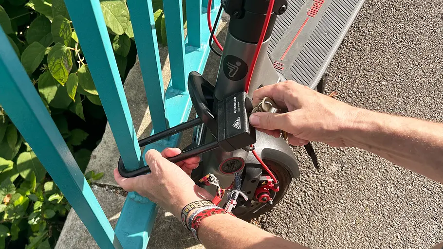 E-Scooter Segway Ninebot F3 Pro D Die Detailaufnahme zeigt die Hand eines Testredakteurs beim Anschließen des E-Scooter Segway Ninebot F3 Pro D an ein Geländer..